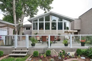 Solarium 4 saisons blanc avec de grandes fenêtres installé sur une terrasse dans un jardin